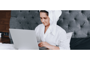 Woman in bathrobe using laptop on bed