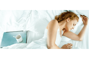 Woman sleeping on bed with laptop and coffee mug next to her